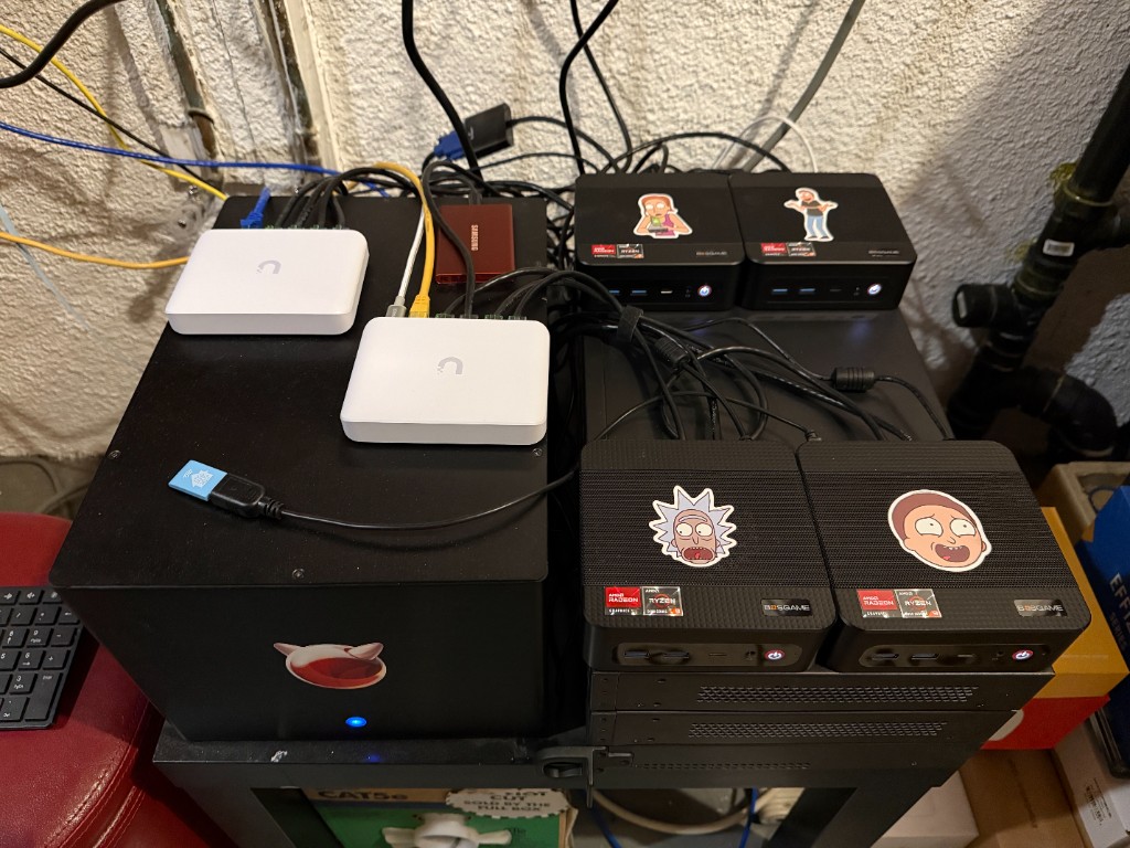 Four BOSGAME Ryzen mini PCs in a rack stack with UniFi switches and a Beastie-sticker chassis, home lab wiring